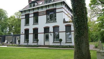 Stately building with a symmetrical facade, featuring a prominent entrance and a porch area with seating.