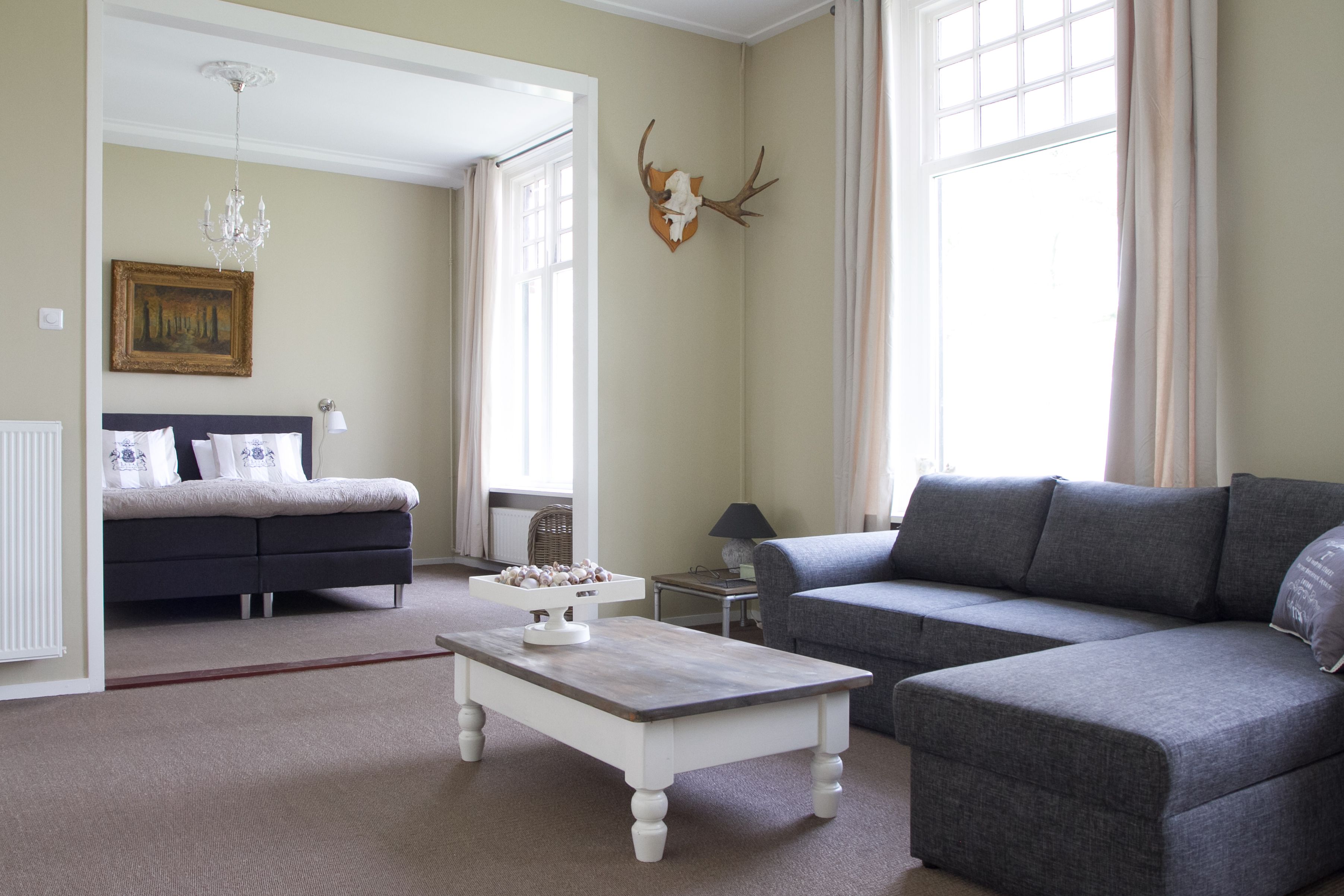A living room with a sofa, a coffee table, a bed, and a chandelier.
