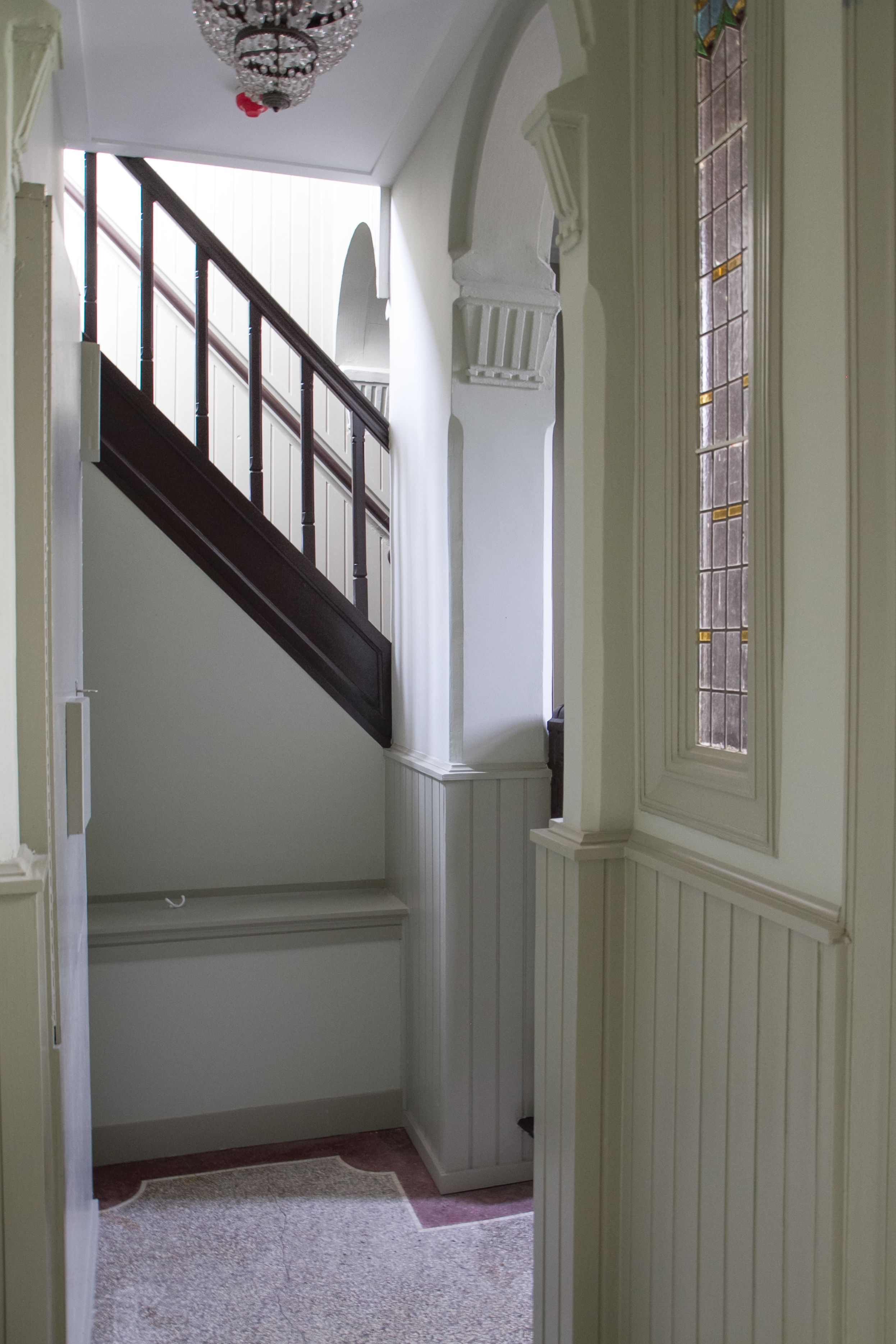 A staircase with white walls and a wooden handrail, leading to a landing with a decorative window.