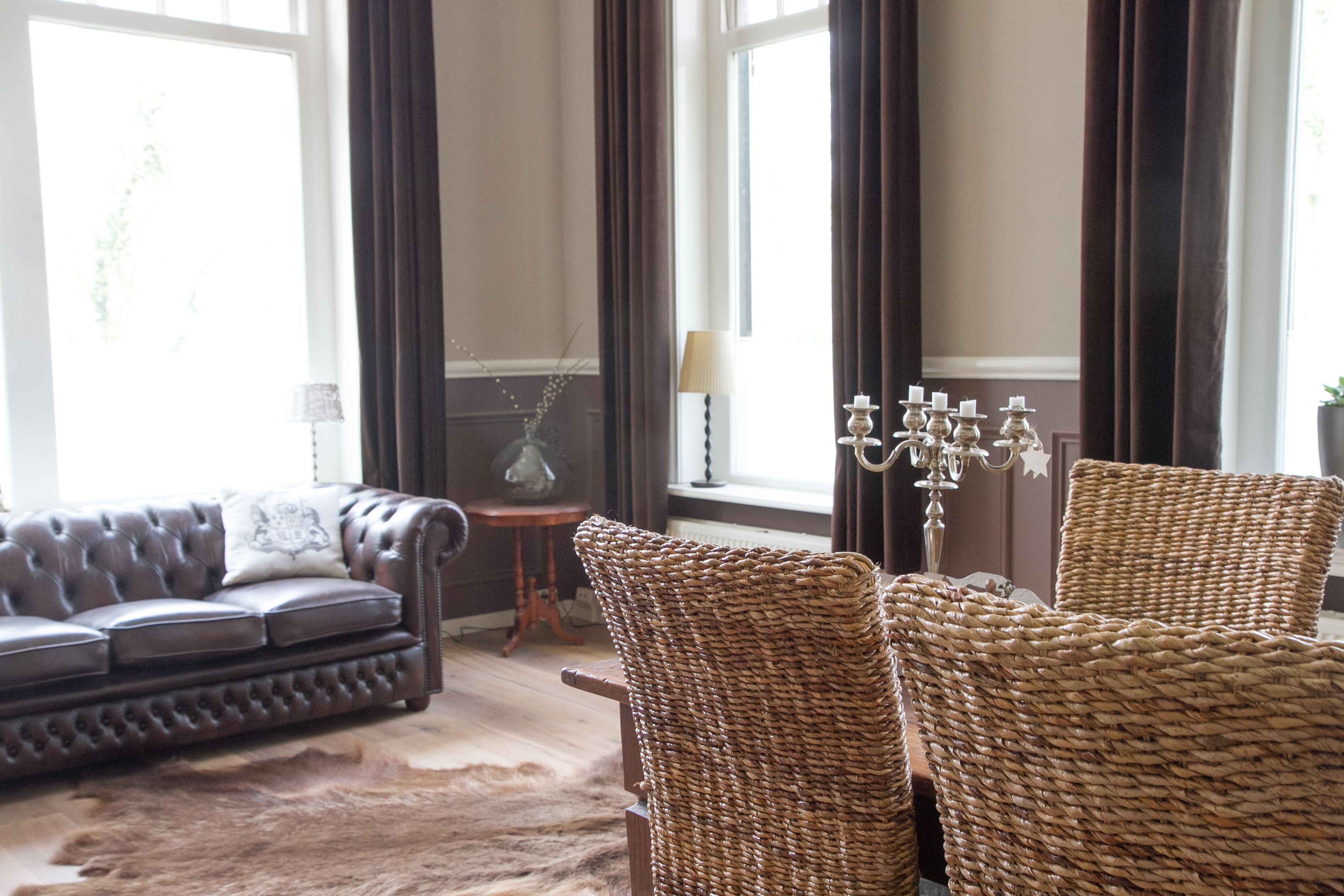 Un salon avec un canapé en cuir, des fauteuils en osier, une petite table d’appoint et une lampe.