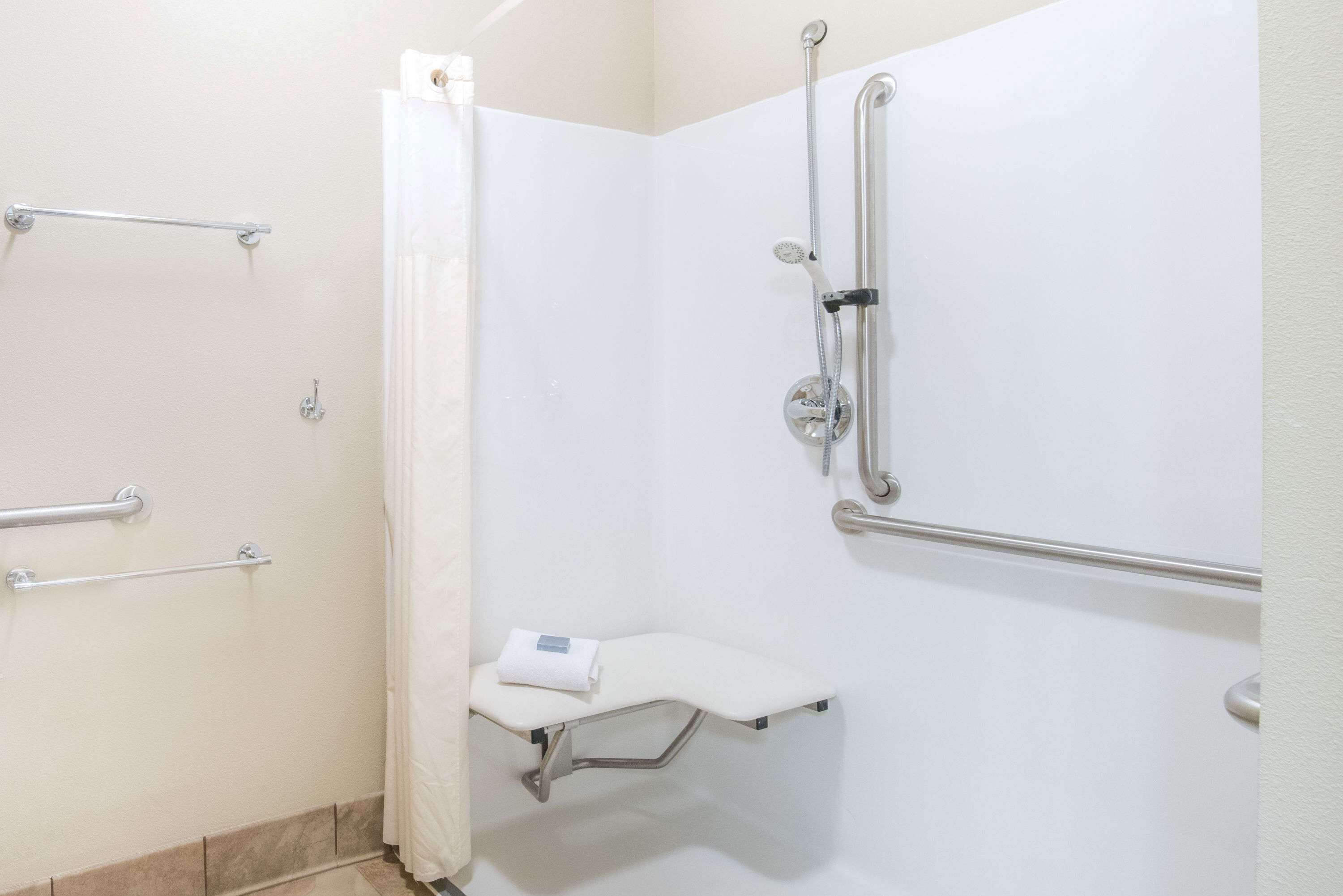 A bathroom with a shower, grab bars, and a bench.