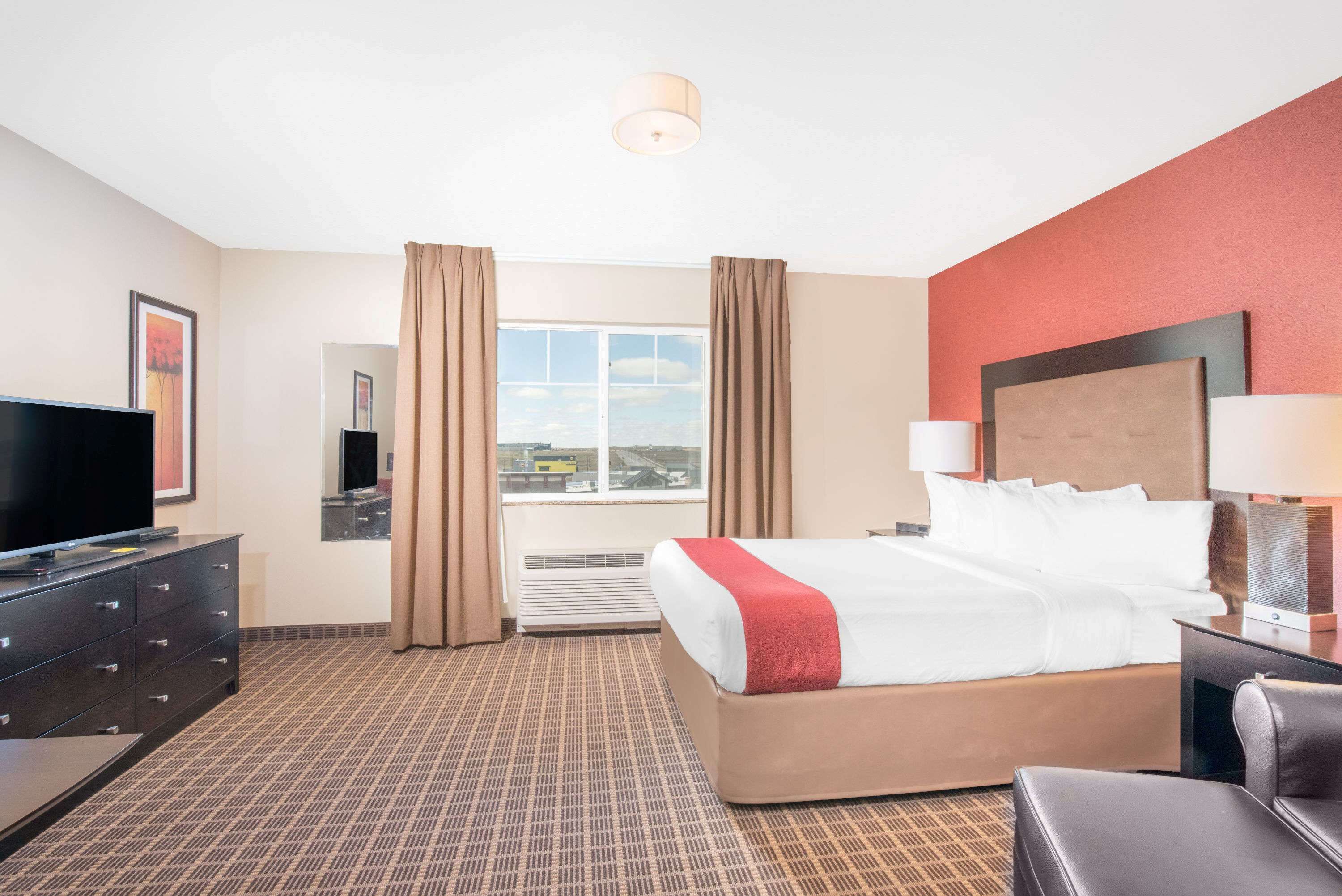 Una habitación de hotel con cama, televisión, escritorio y ventana con cortinas.