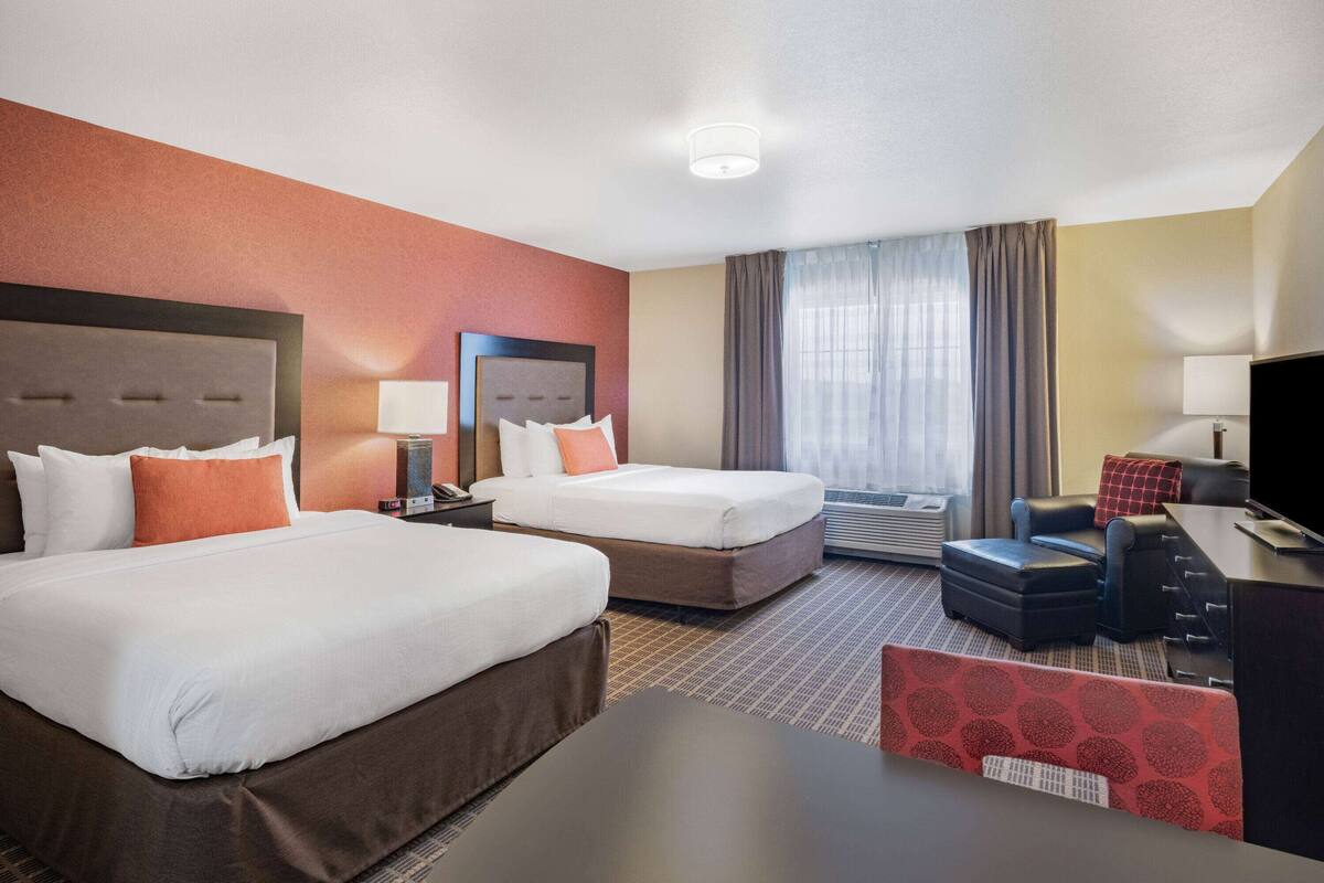 Habitación de hotel con dos camas, un escritorio, una silla, un televisor y una ventana con cortinas.