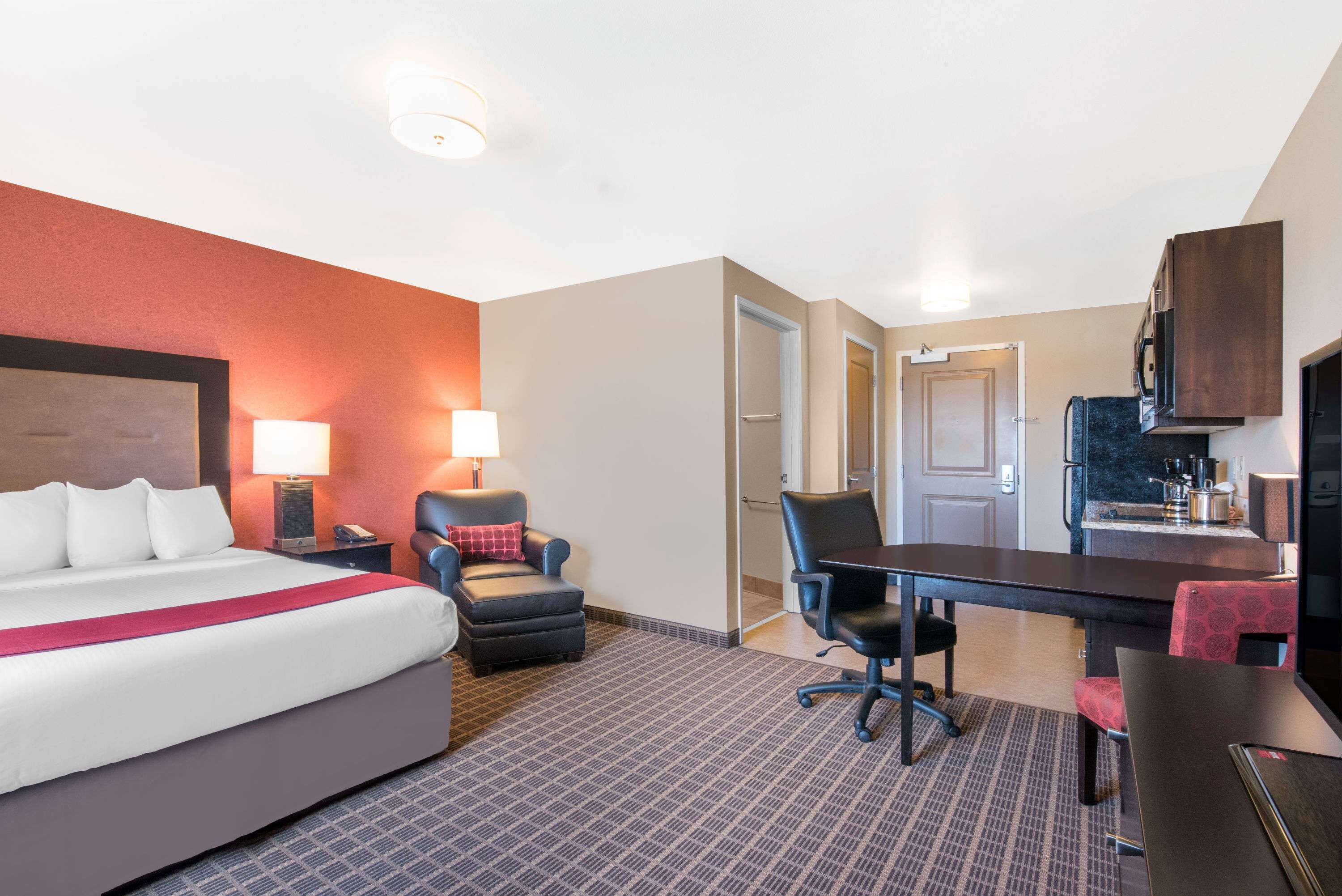 Una habitación de hotel con una cama grande, un escritorio, una silla, una lámpara y una kitchenette.