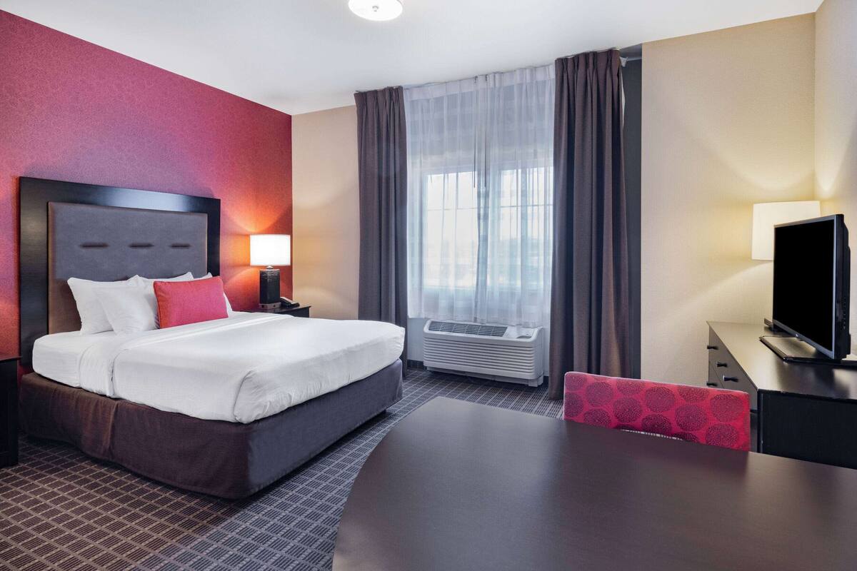 Habitación de hotel con cama, mesitas de noche, escritorio, silla, aire acondicionado y televisor.
