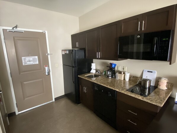 Una cocina compacta con armarios de madera oscura, un refrigerador negro, un microondas y un lavavajillas.