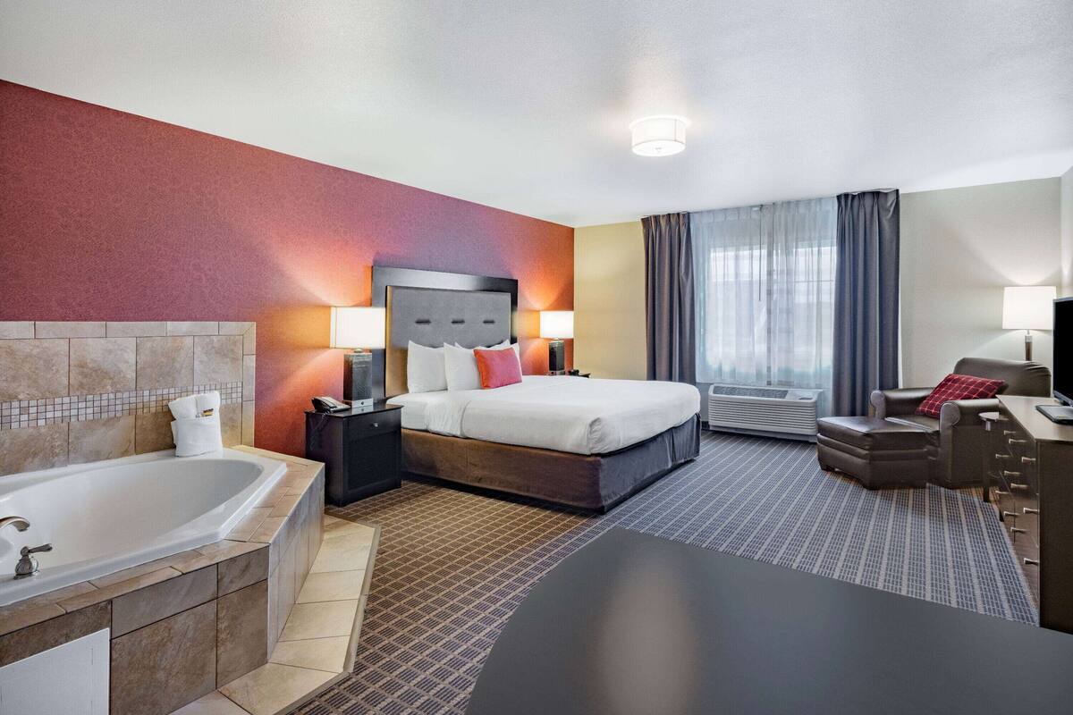 Una habitación de hotel con una cama grande, baño privado con bañera, escritorio y una silla.