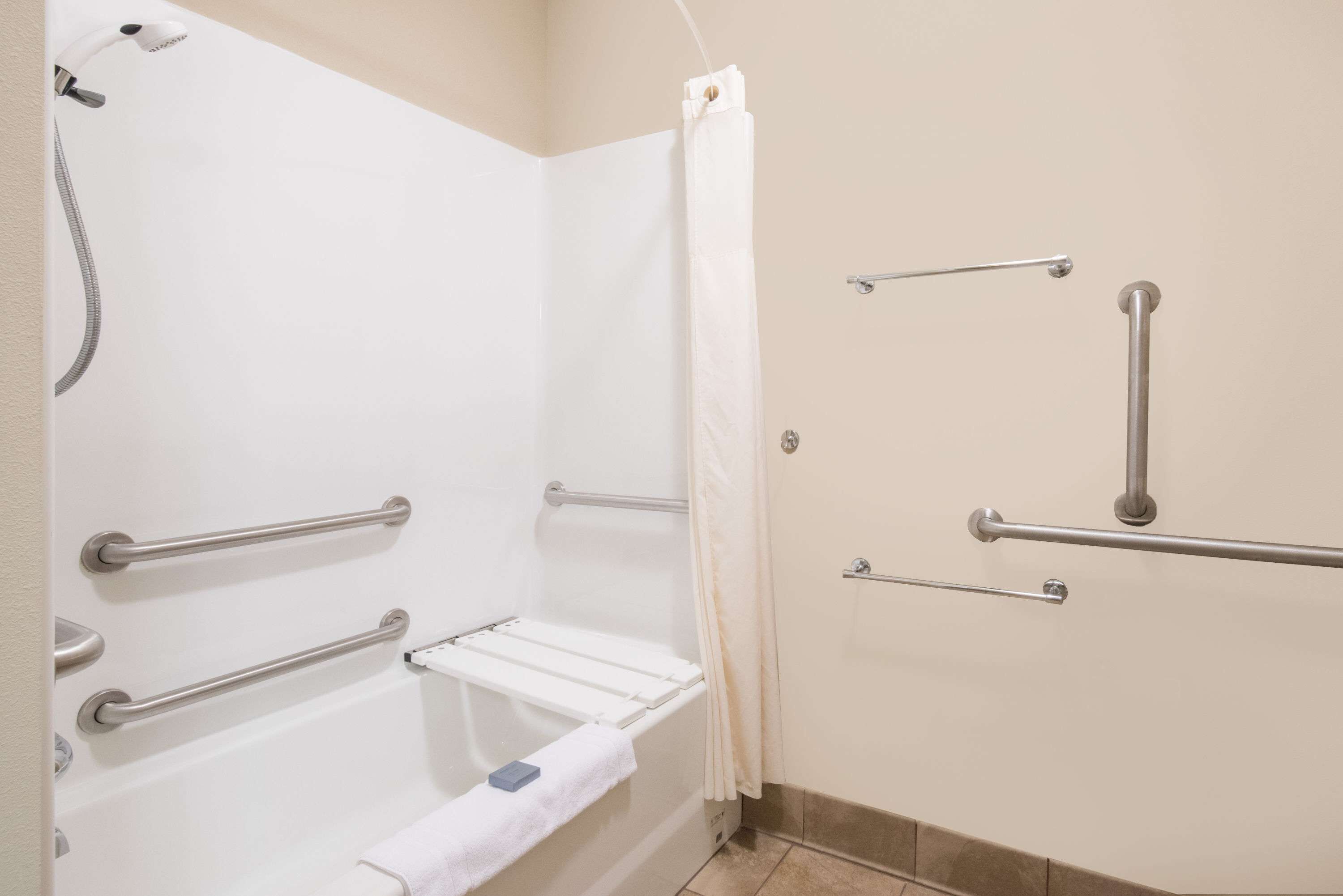 Un baño con cabina de ducha, barras de apoyo y un perchero.