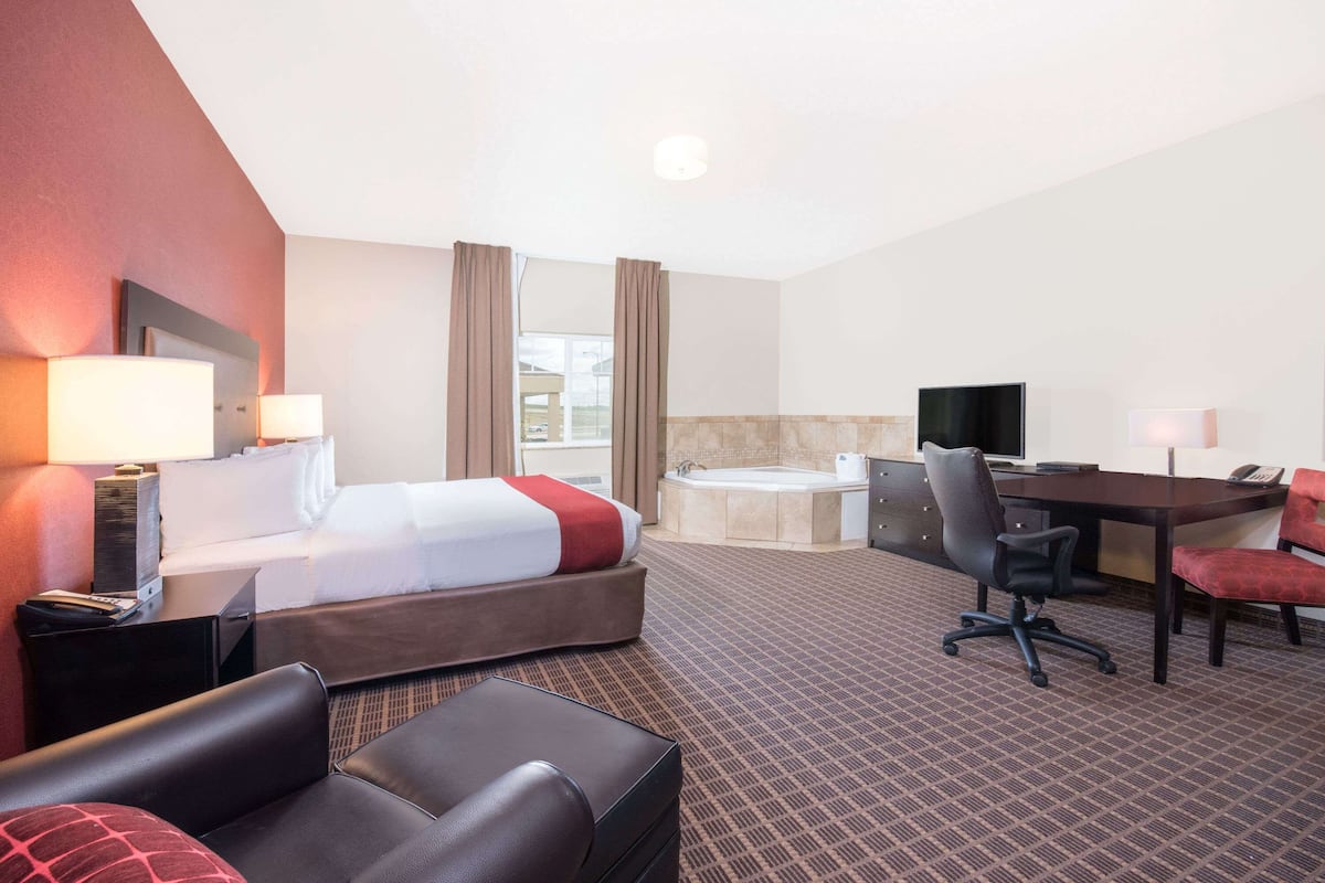 Habitación de hotel con cama, escritorio, silla, televisión y baño con bañera.