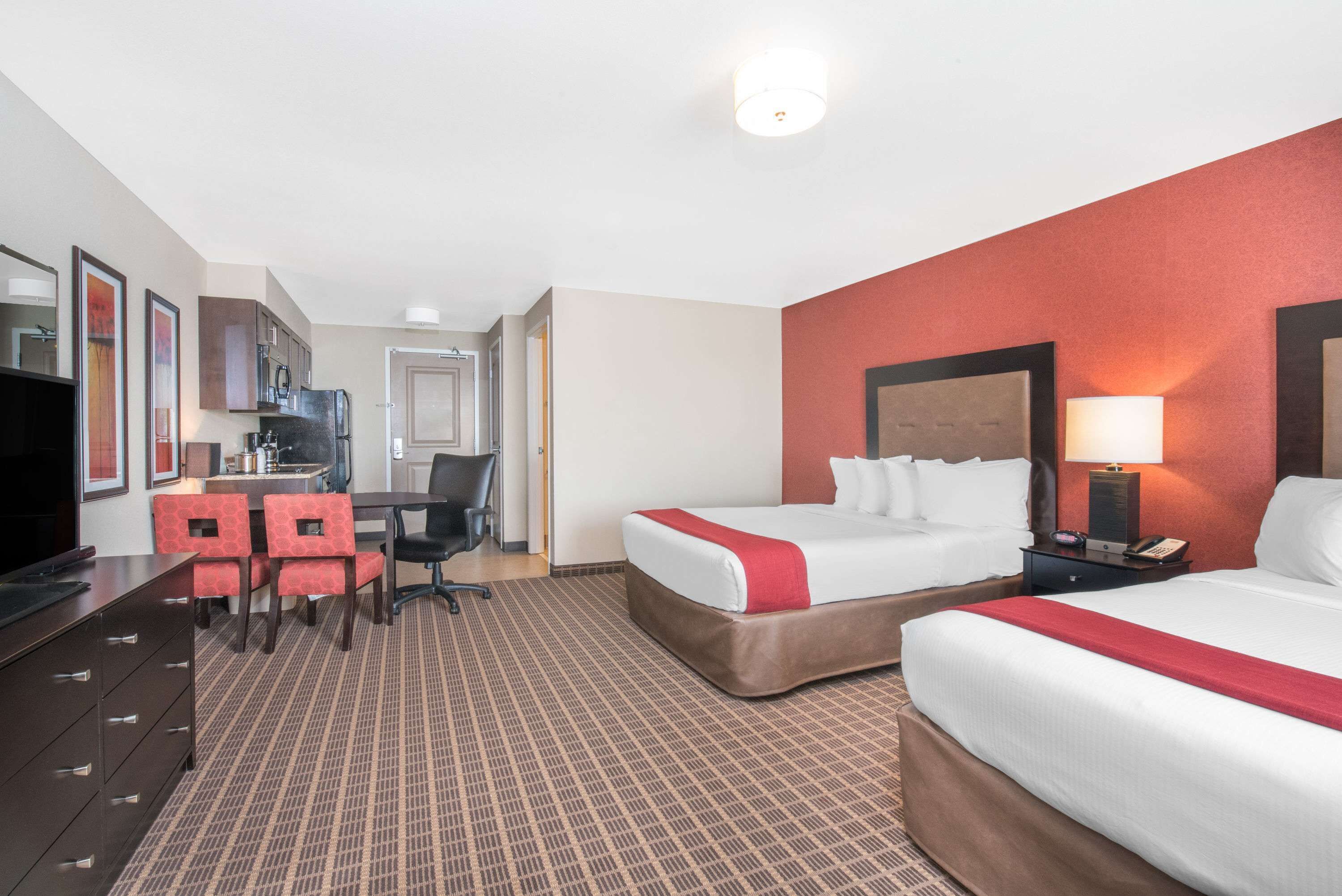 A hotel room with two beds, a desk with a chair, a television, and a kitchenette.