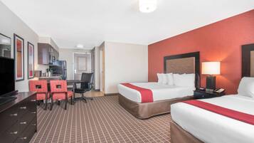 A hotel room with two beds, a desk with a chair, a television, and a kitchenette.