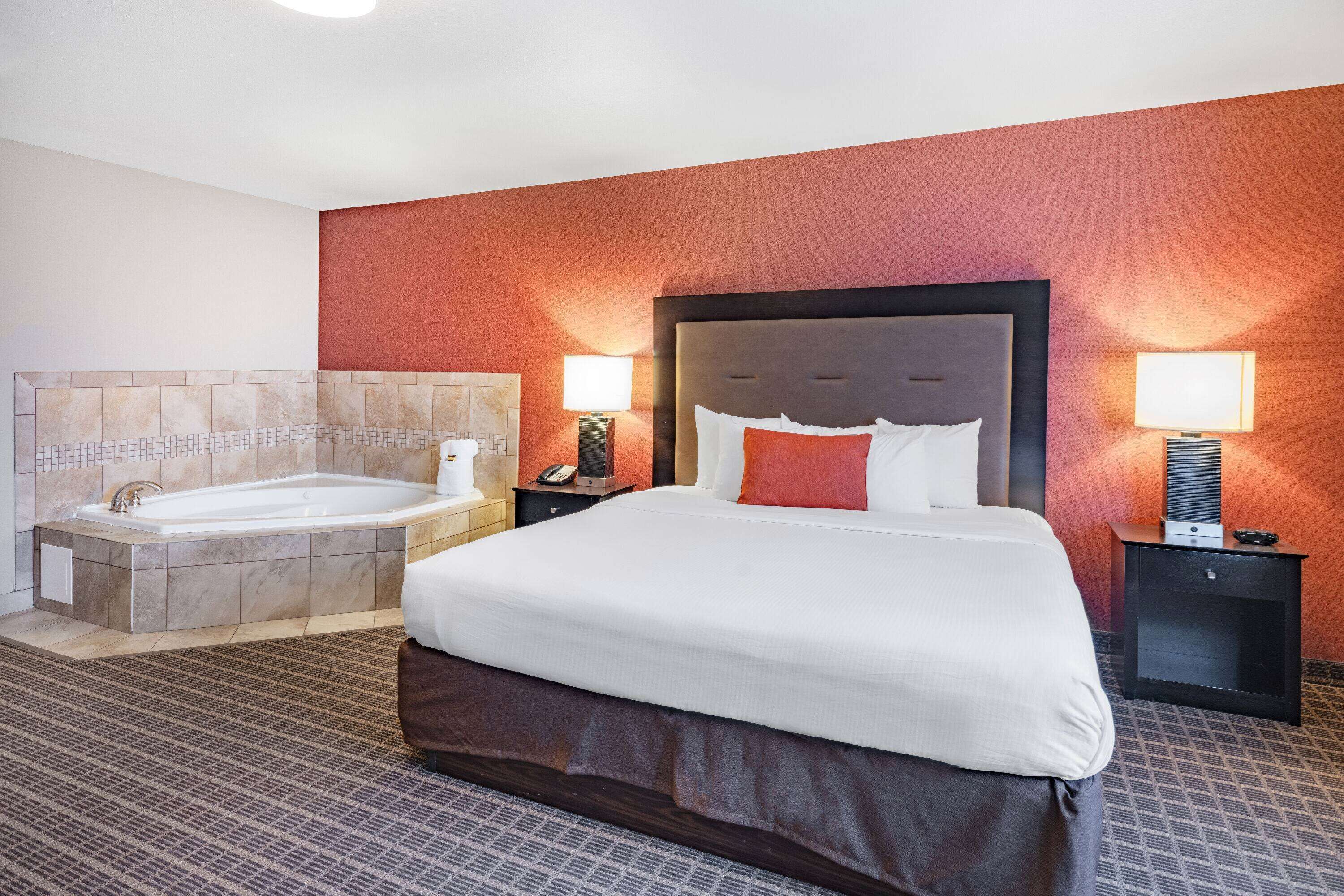 A hotel room with a large bed, a separate bathroom with a bathtub, and two bedside tables with lamps.
