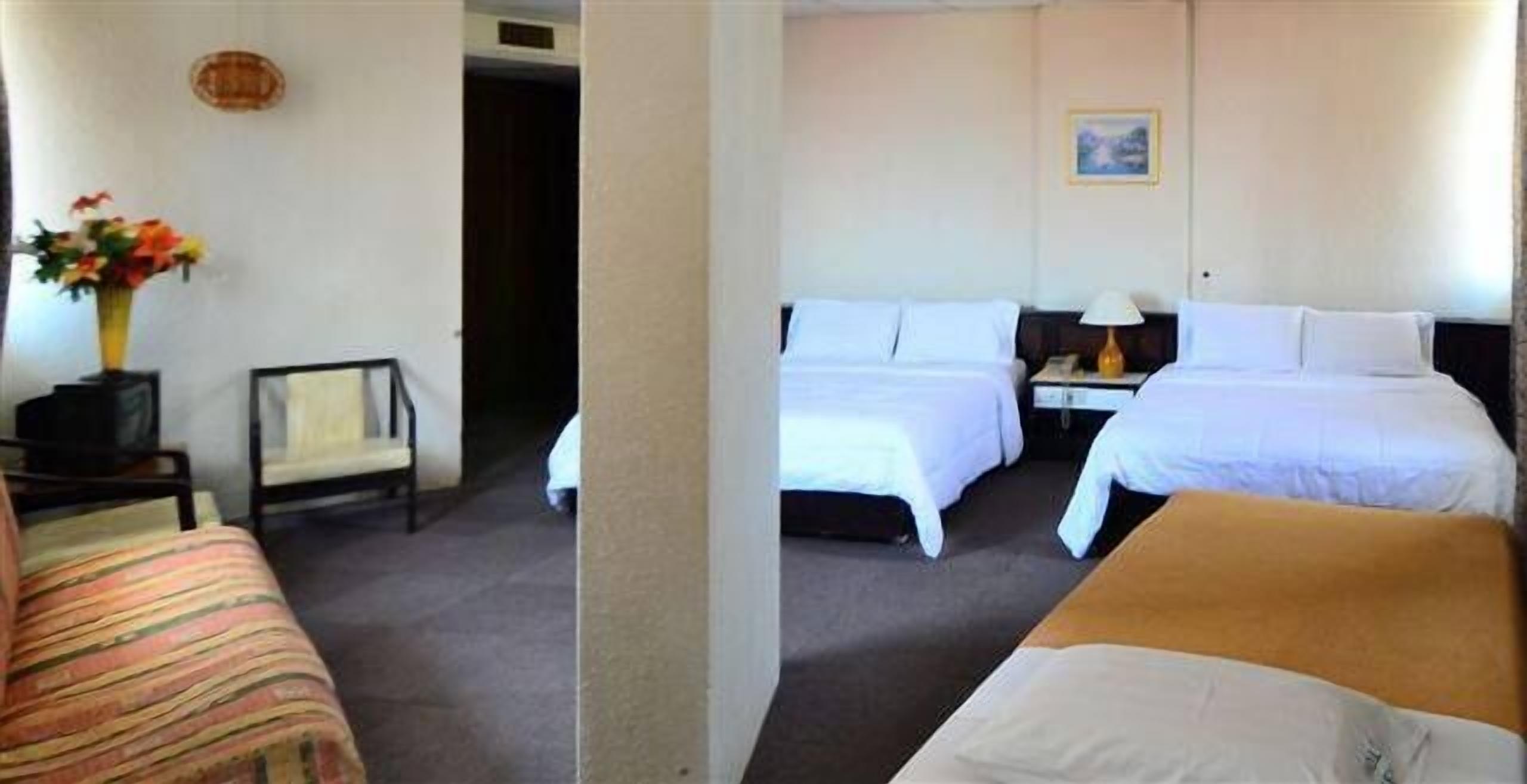 A hotel room with two beds, a chair, a desk, and a vase of flowers.