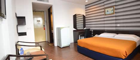 Ein Hotelzimmer mit Bett, Schreibtisch, Stuhl, Kühlschrank und einem Bild an der Wand.