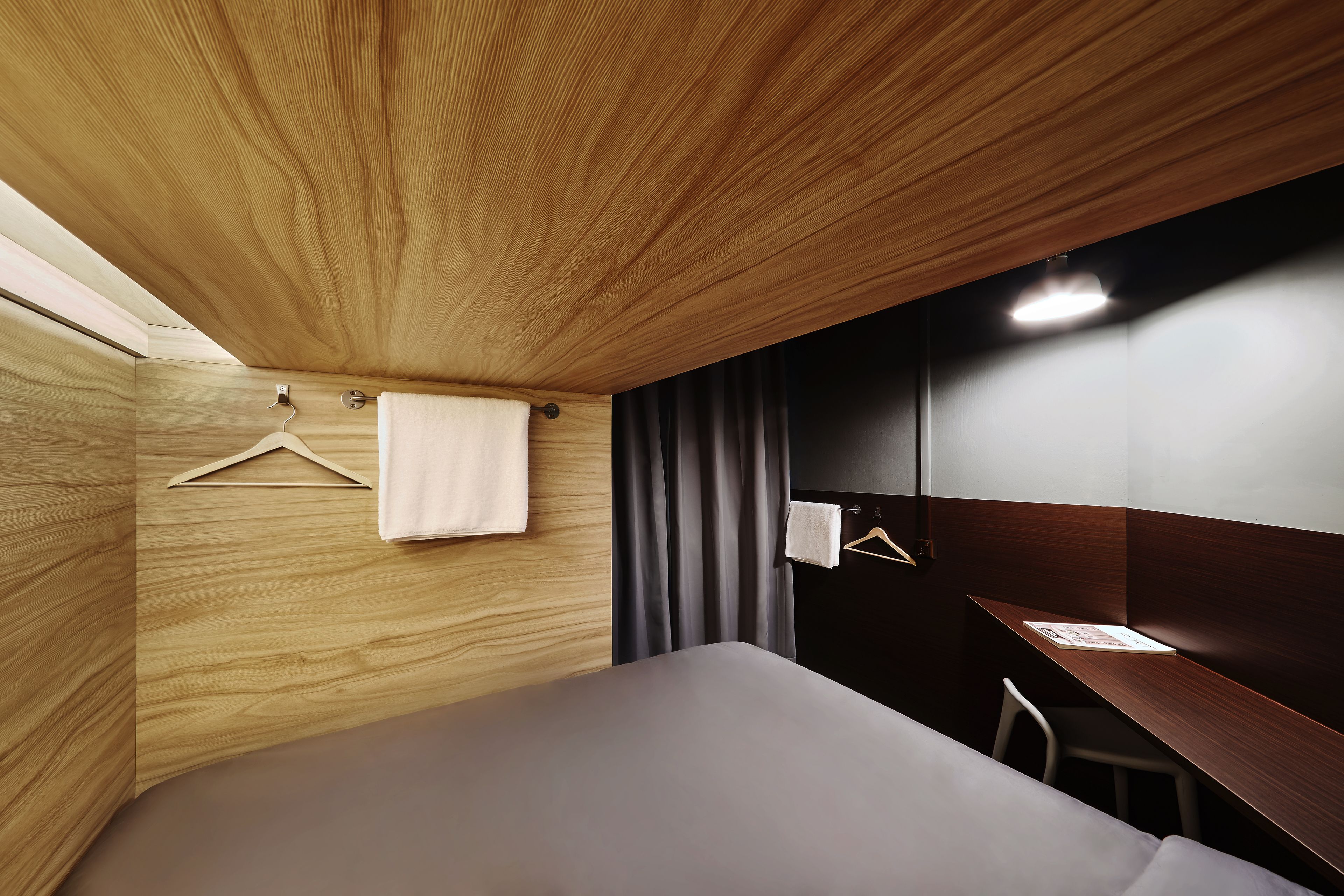 A modern hotel room with a wooden ceiling, a bed, a desk, and a chair.