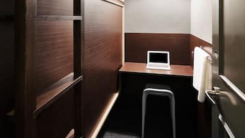 Quarto compacto e moderno com escrivaninha de madeira, um laptop, luminária pendente e um banquinho pequeno.