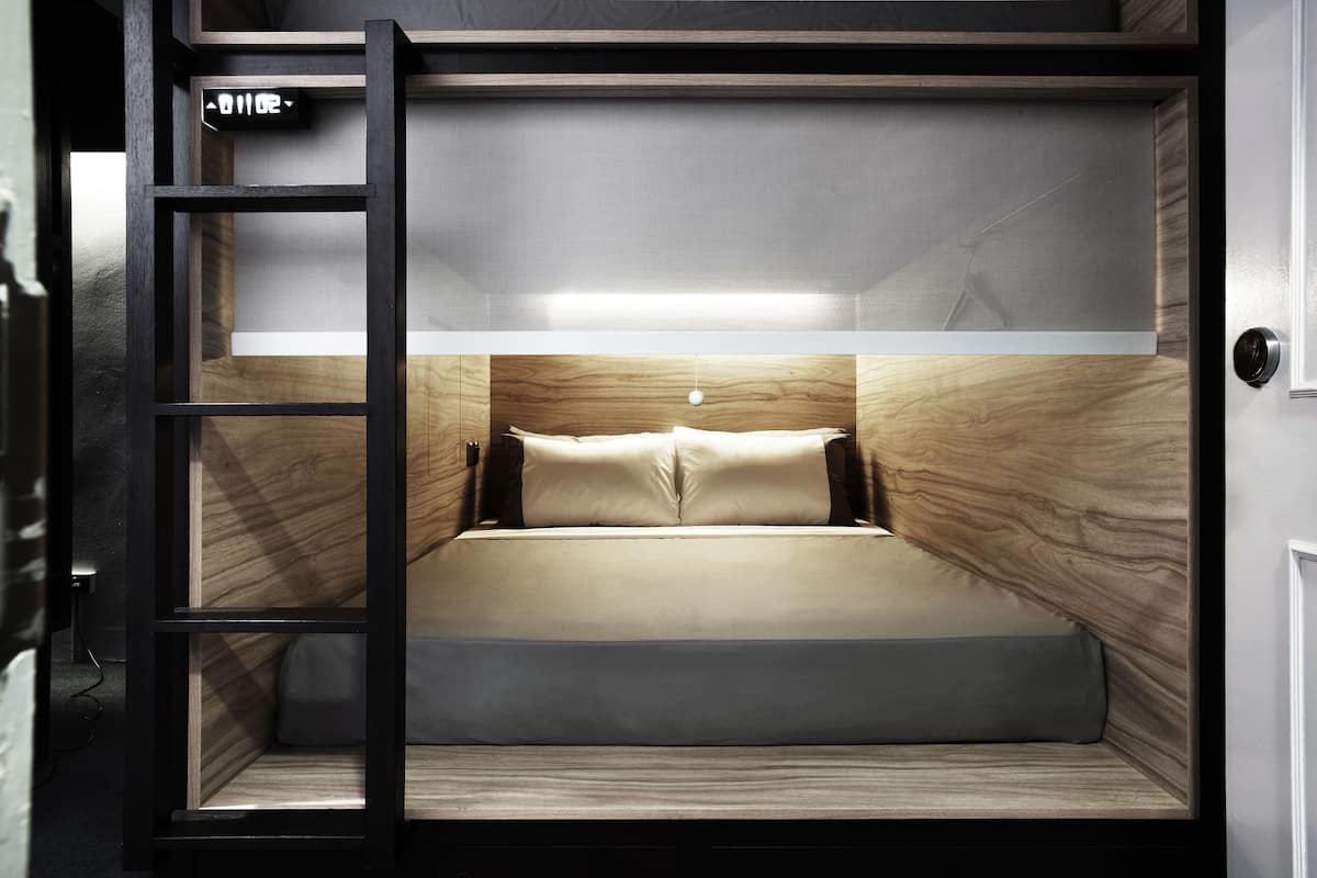 A bunk bed with a ladder, a small shelf, and a wall-mounted light.