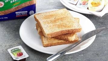 A plate with two slices of wholemeal bread, a knife, and a container of Heinz ketchup.