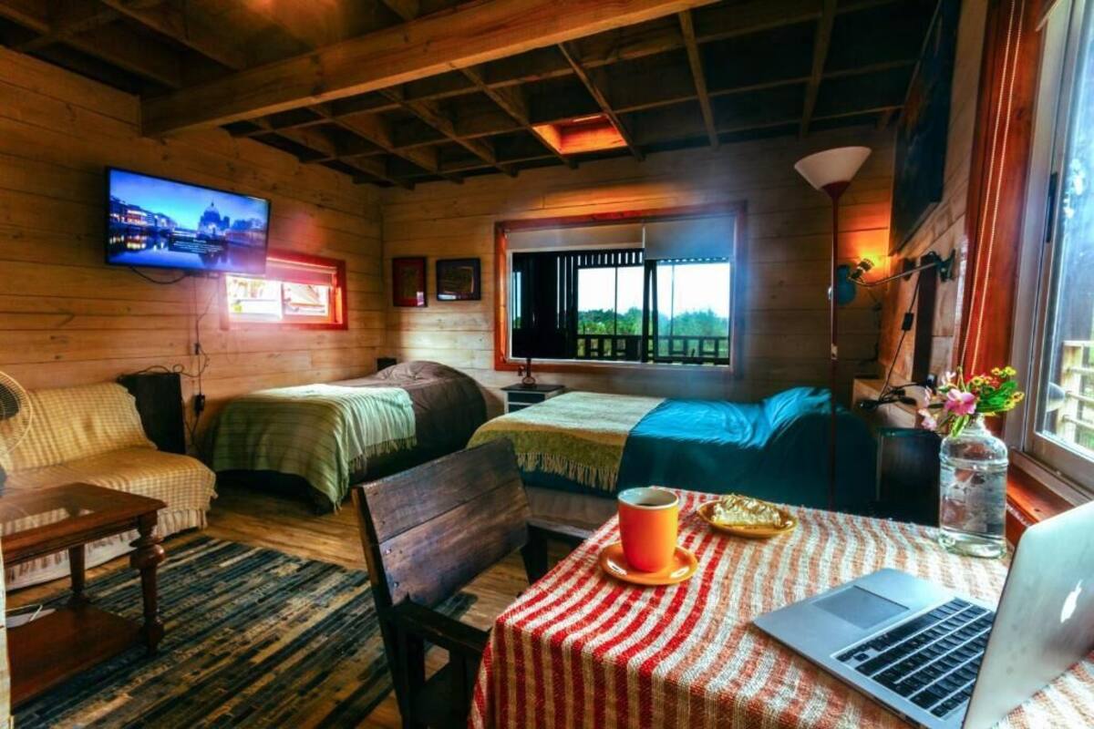 Una habitación acogedora con dos camas, una laptop sobre una mesa y un televisor en la pared.