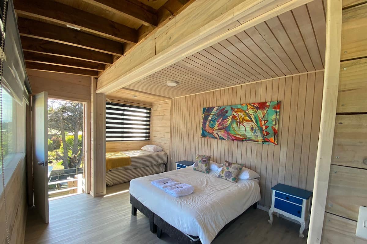 Una habitación de madera con una cama, un banco y un cuadro abstracto y colorido.