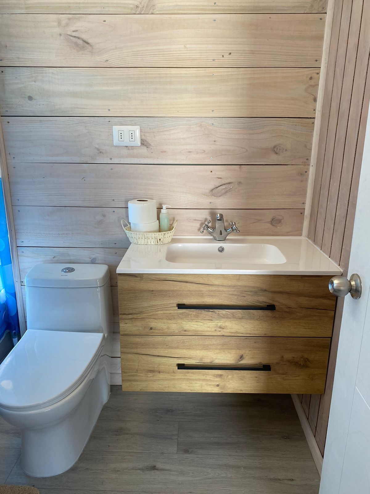 A compact bathroom with a wooden vanity, a toilet, and a sink.