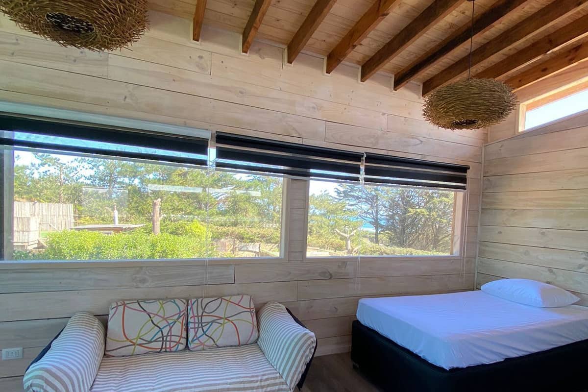 Un dormitorio con techo de madera, un sofá, una cama y un ventanal con vistas a la vegetación.