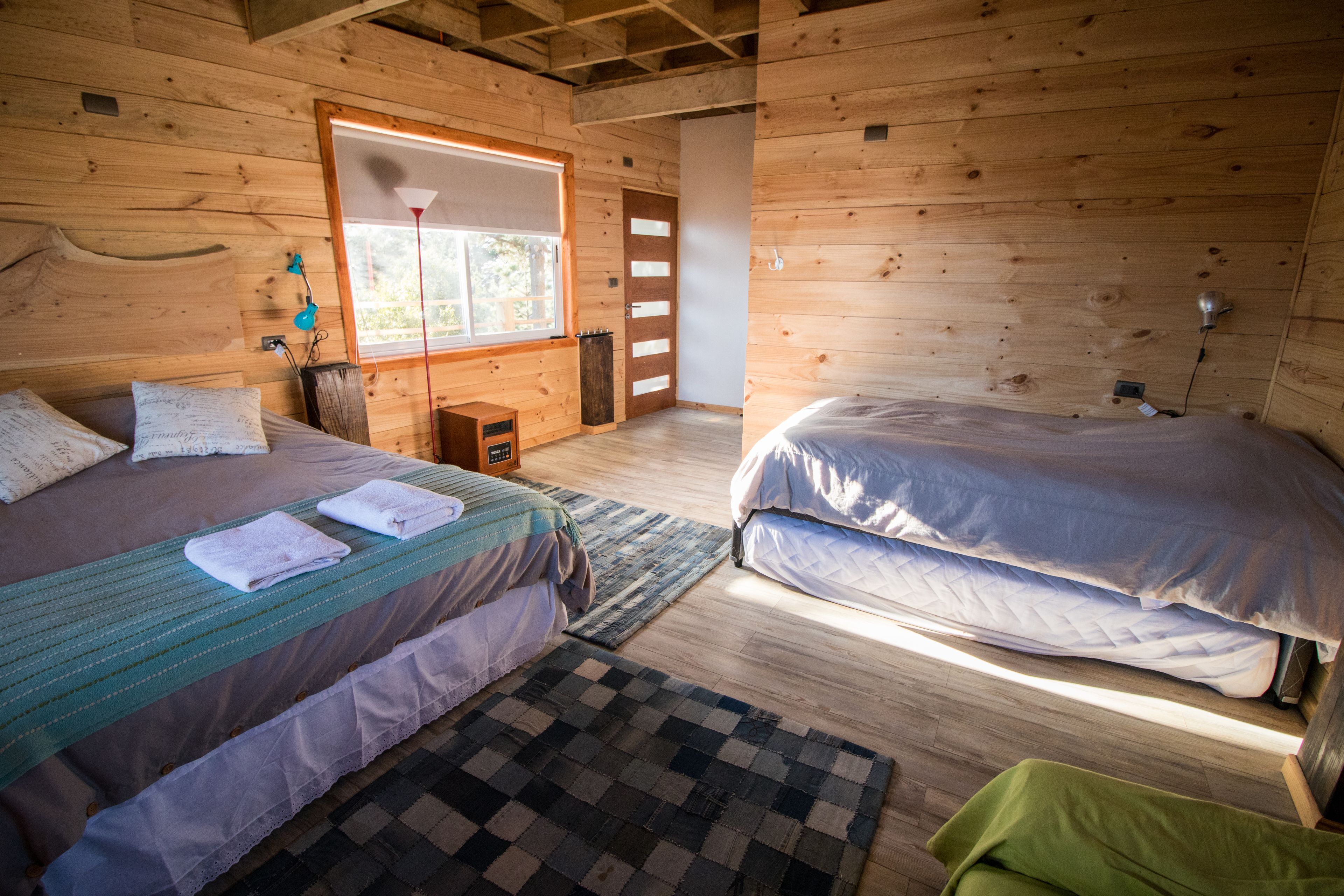 Een slaapkamer in een houten blokhut met twee bedden, een raam en een klein tafeltje.