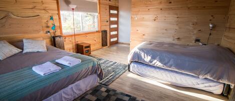 Een slaapkamer in een houten blokhut met twee bedden, een raam en een klein tafeltje.