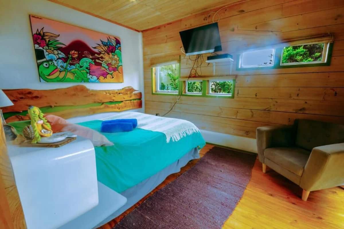Una habitación acogedora con una cama, un televisor en la pared y un ventanal con vistas a zonas verdes.