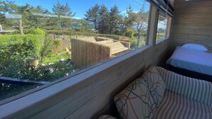 Een kamer met houten plafond, een raam met uitzicht op een tuin, en een bed met een gestreept kussen.