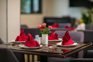 Una mesa de comedor con servilletas rojas, cubiertos y un florero con flores.