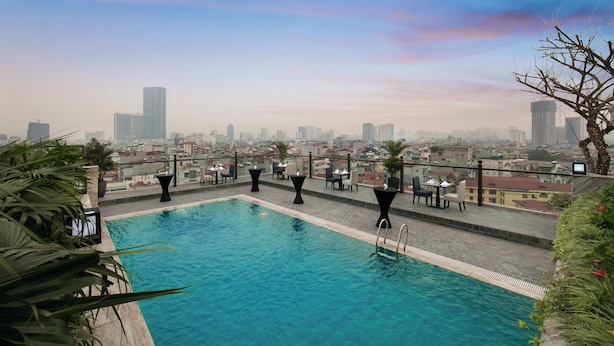 Una piscina en la azotea con vistas a la ciudad, rodeada de palmeras y mobiliario moderno.
