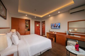 A hotel room with a bed, a desk, a TV, and a small table with a bottle and glasses. - Sen Luxury Hotel (Hanoi)