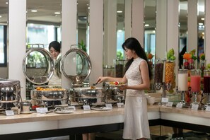 A buffet area with various food stations and a person serving themselves.