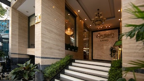 Entrada de hotel con pared de mármol, un cartel que dice "Sen Hotel 2 Luxury" y un candelabro.