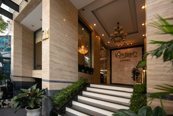 Entrada de hotel con pared de mármol, un cartel que dice "Sen Hotel 2 Luxury" y un candelabro.