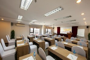 Una sala de conferencias con mesas, sillas y una pantalla para presentaciones.