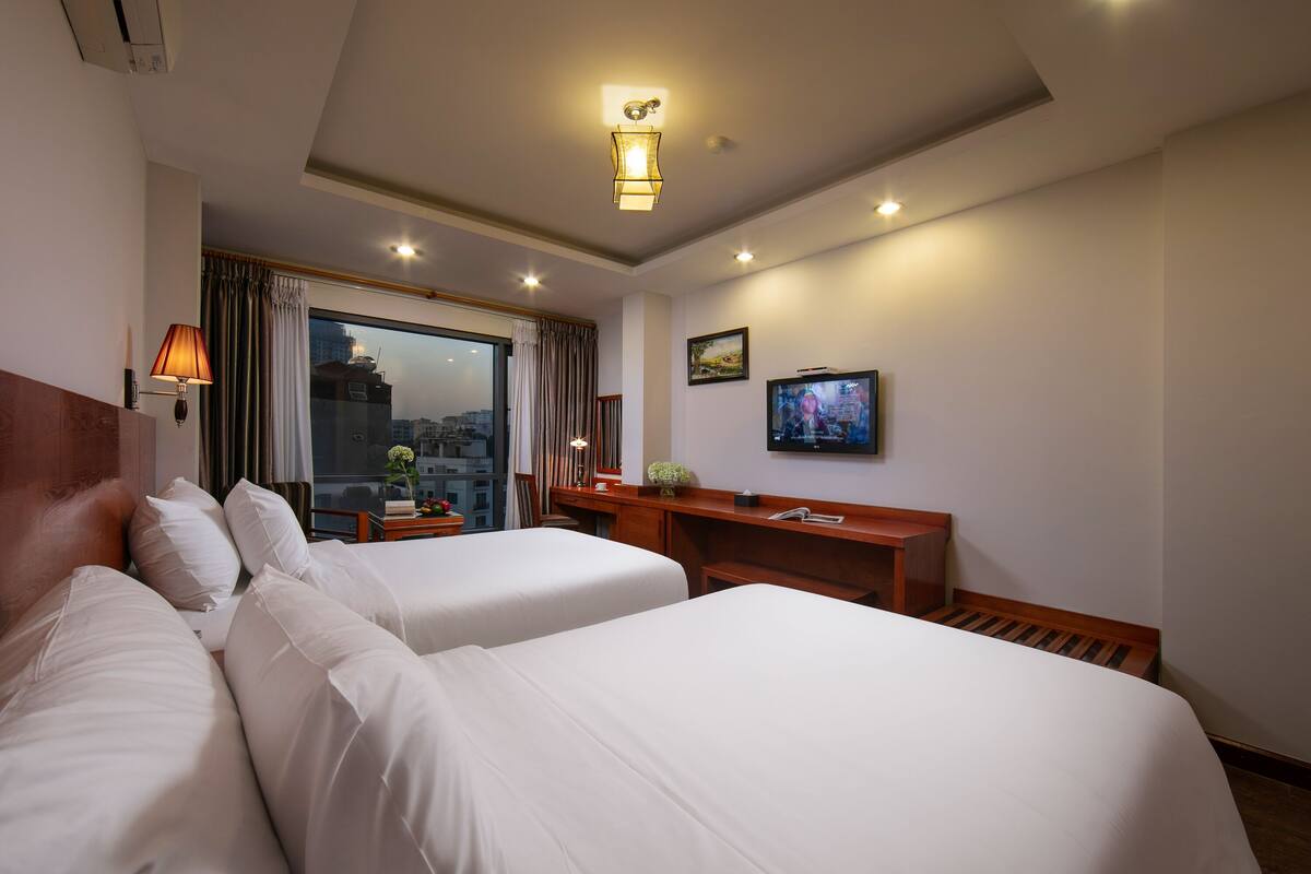 A hotel room with two beds, a desk, a television, and a window with curtains.