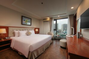 Habitación de hotel con una cama grande, un escritorio, una silla, un televisor y vistas a la ciudad.