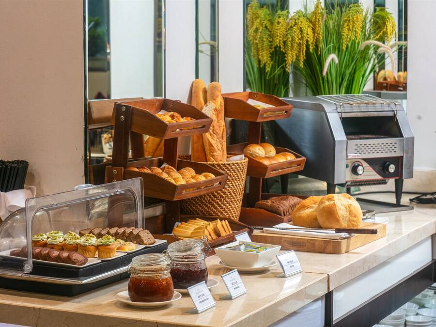 Un bufé con diversos productos de panadería, como pan, muffins y pasteles, con una máquina de café y una variedad de aderezos.