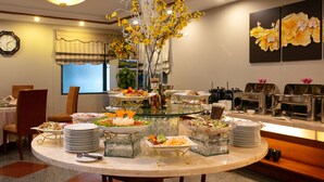 A buffet setup with various dishes, a clock, and decorative elements like flowers and paintings. - Sen Hotel (Hanoi)