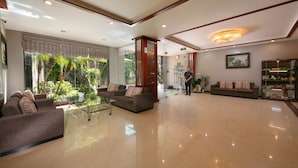 A spacious lobby with a large sofa, a coffee table, and a glass partition. There is a chandelier, a clock, and a framed picture on the wall. - Sen Hotel (Hanoi)