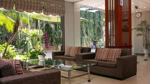 A modern lounge area with two sofas, a glass coffee table, and a large window with tropical plants. - Sen Hotel (Hanoi)