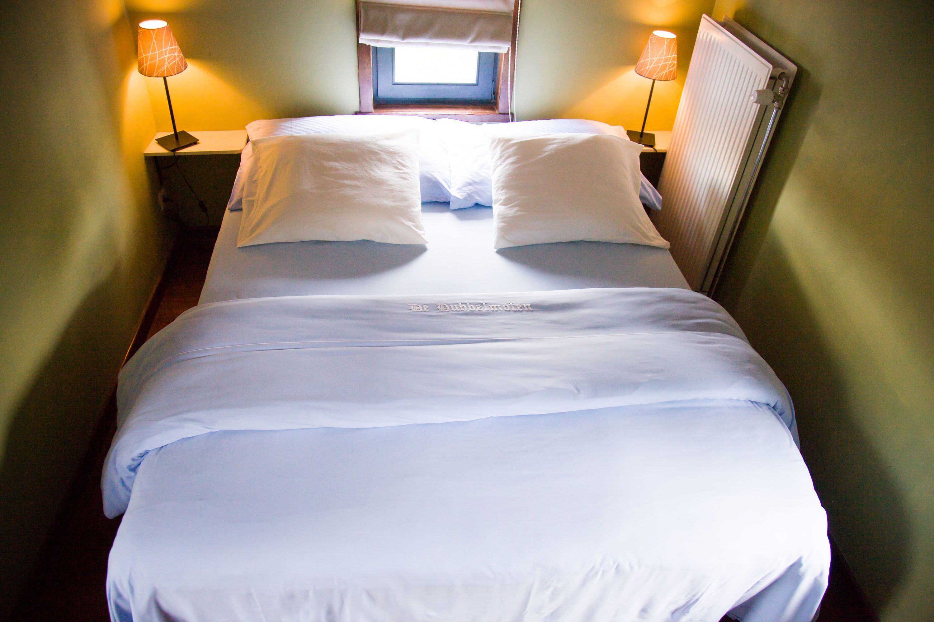 A neatly made bed with white linens, two bedside lamps, and a window above the bed.