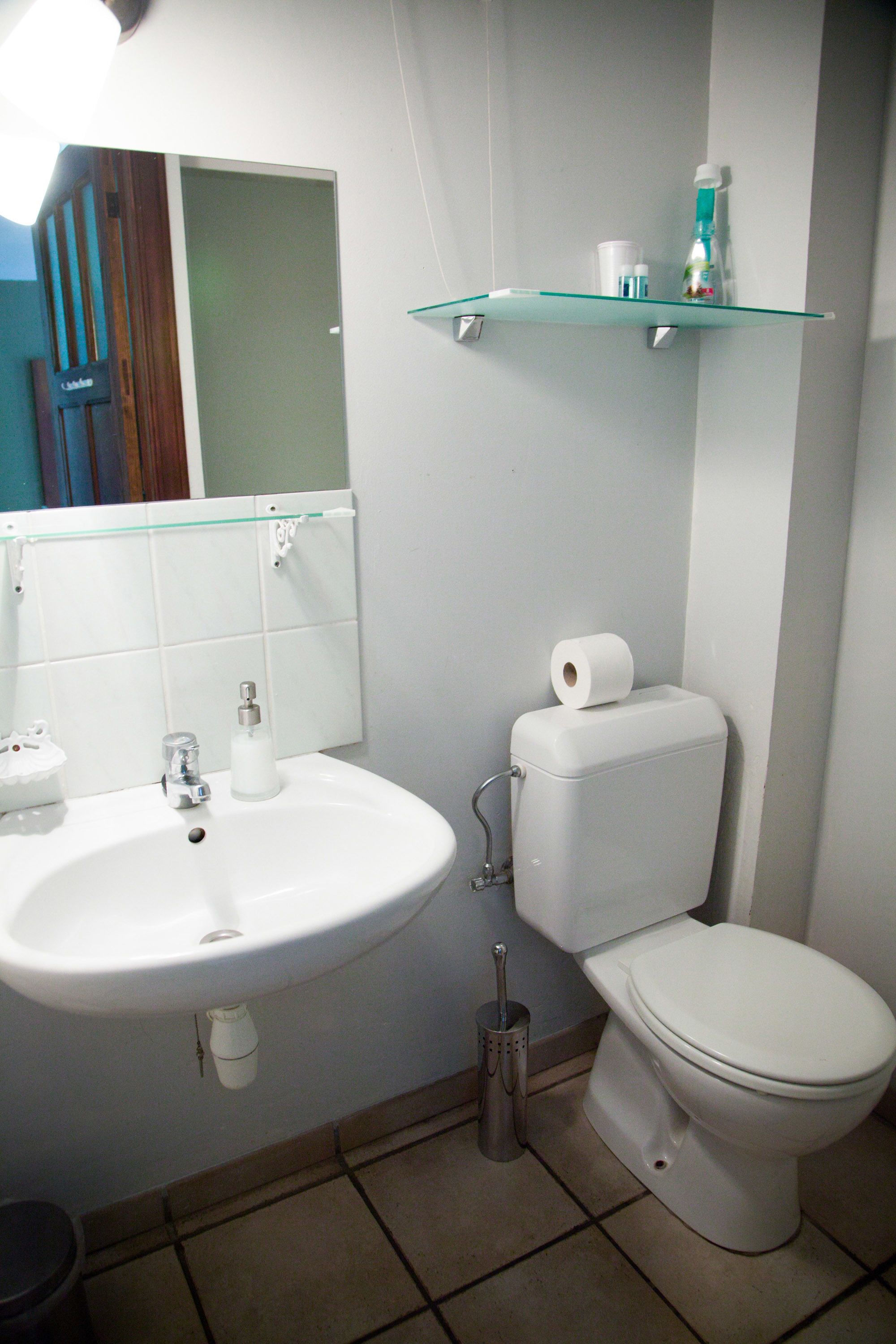 A bathroom with a white sink, toilet, and glass shelf above the toilet.