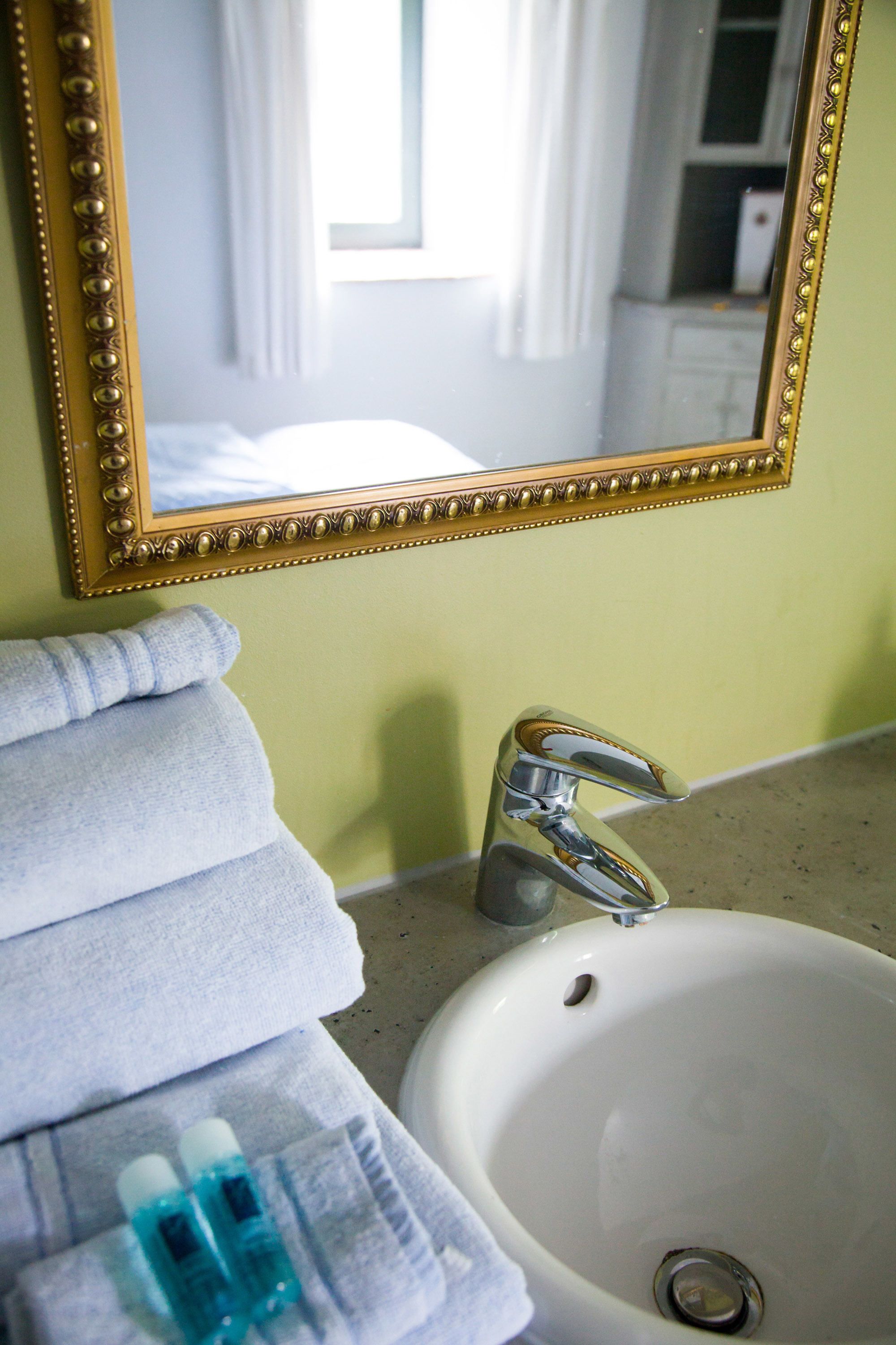 A bathroom with a white sink, a gold-framed mirror, and stacked towels.