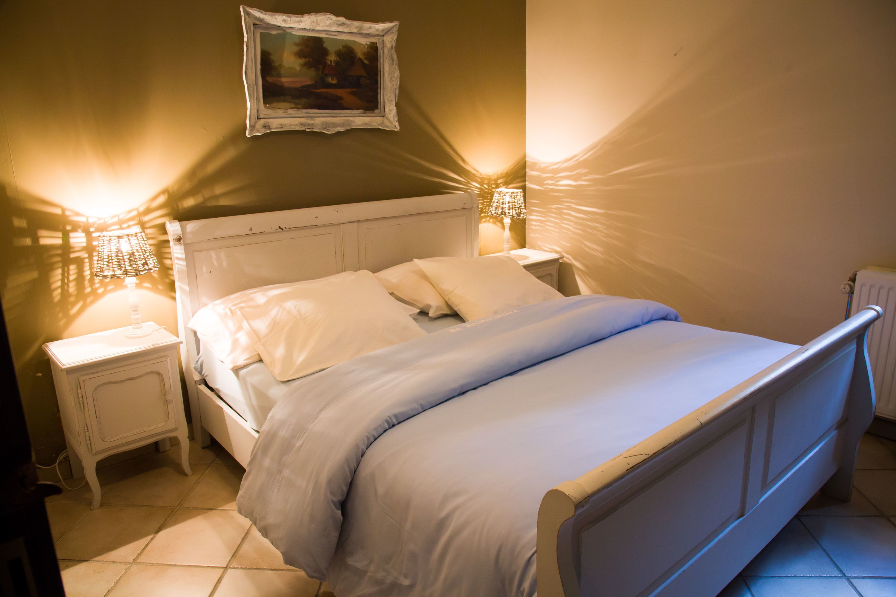 Una cama bien hecha con ropa de cama blanca, un cabecero blanco y dos mesitas de noche con lámparas.