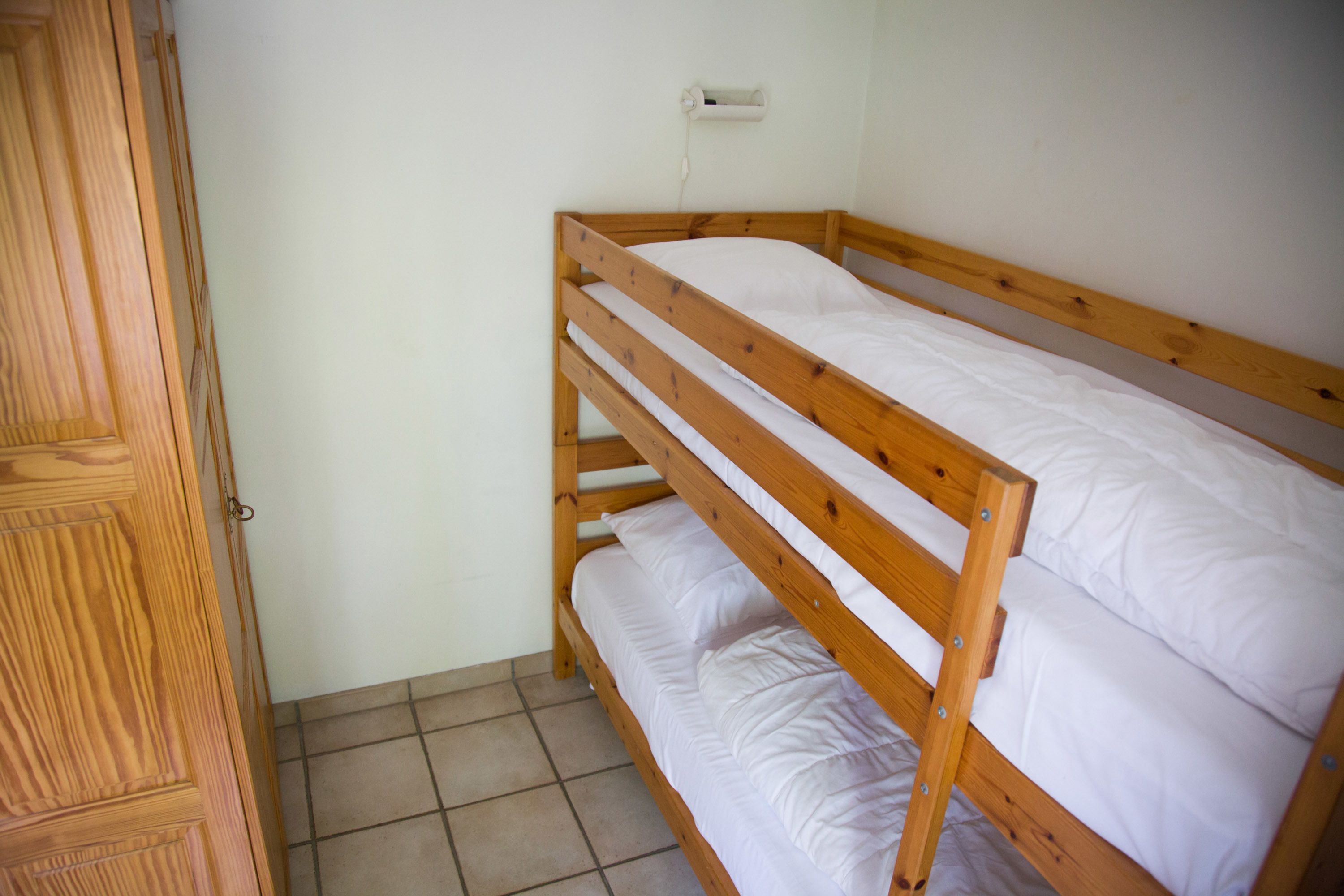 A bunk bed with white bedding in a room with a wooden door and a white wall.