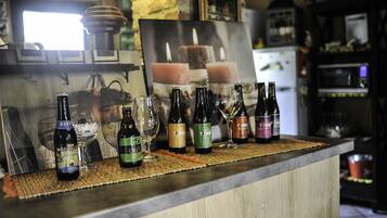 A bar counter with various bottles and glasses, a framed picture of candles, and a rustic kitchen background.