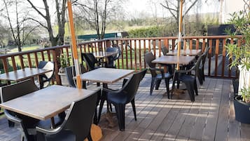 Enjoy dining or socializing in this outdoor patio area with tables and chairs, surrounded by lush greenery and a garden view.